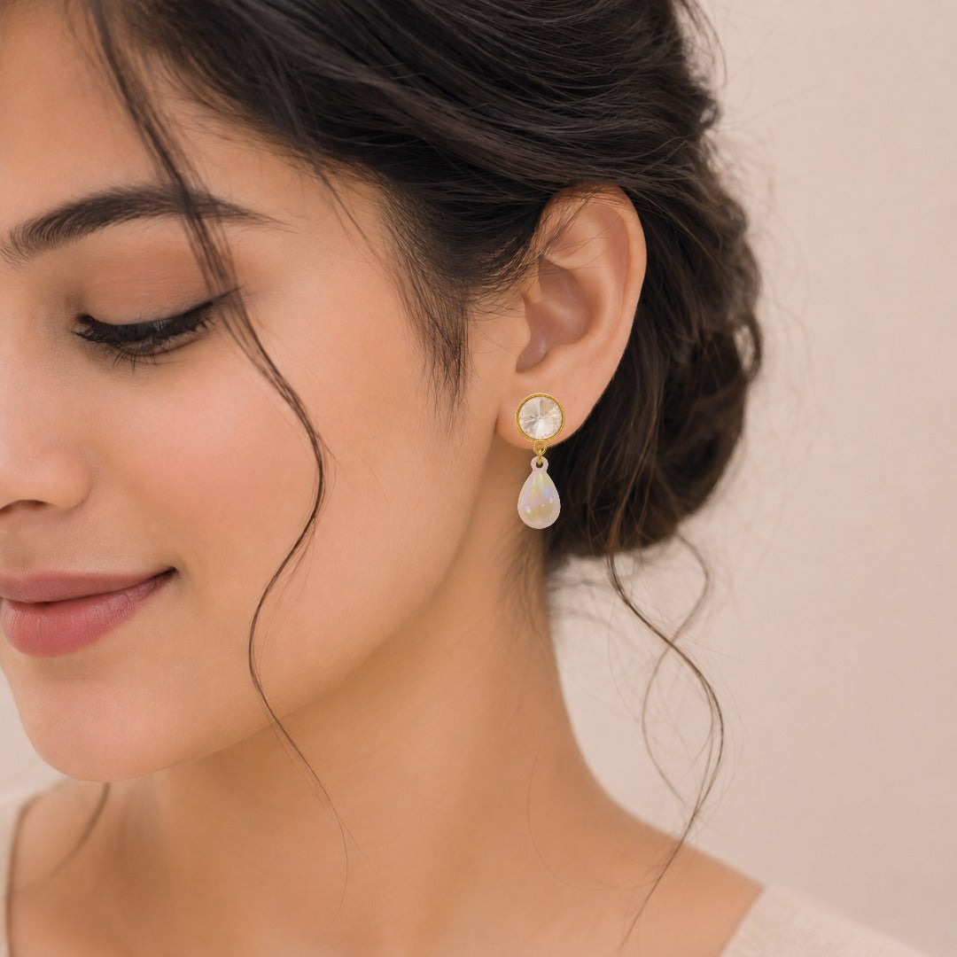 A close-up of a woman wearing elegant crystal pearl drop earrings with gold-tone crystal studs and iridescent teardrop faux pearls.