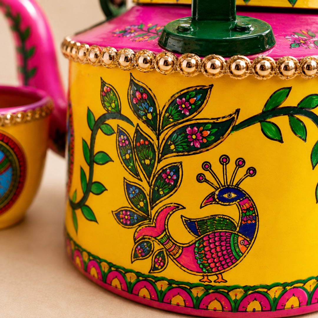 A close-up of ahaeli brightly painted teapot with a yellow body, pink lid, green handle, and colorful peacock and floral motifs.