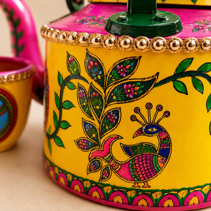 A close-up of ahaeli brightly painted teapot with a yellow body, pink lid, green handle, and colorful peacock and floral motifs.