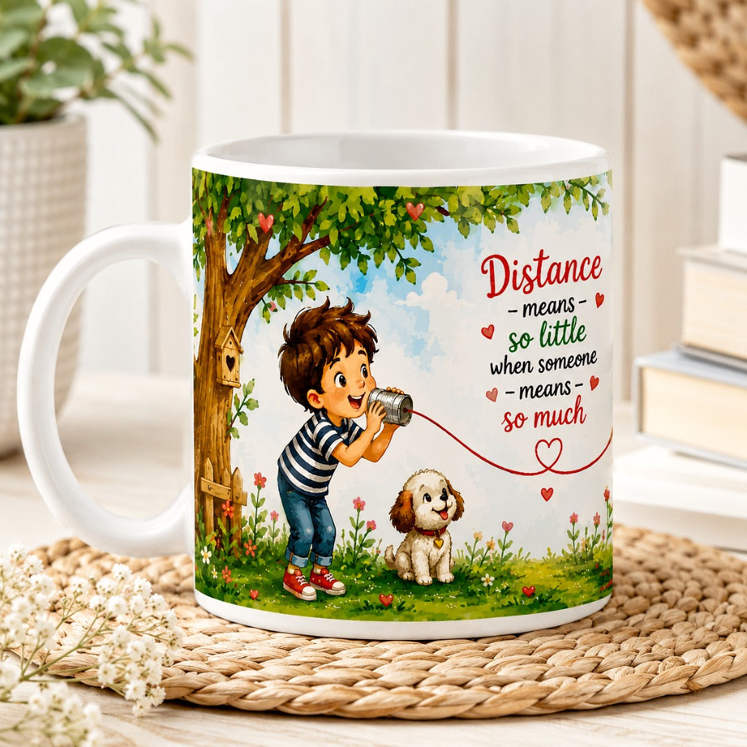 Front view of the Distance Means So Little Coffee Mug featuring a boy speaking through a tin can telephone, connected to a girl by a heart-shaped string on a white ceramic mug.