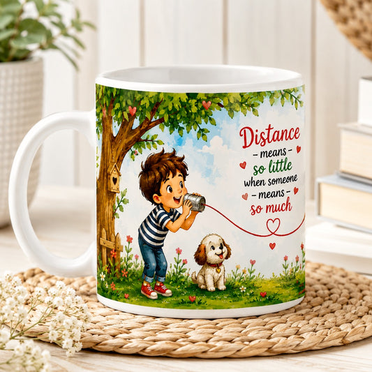 Front view of the Distance Means So Little Coffee Mug featuring a boy speaking through a tin can telephone, connected to a girl by a heart-shaped string on a white ceramic mug.