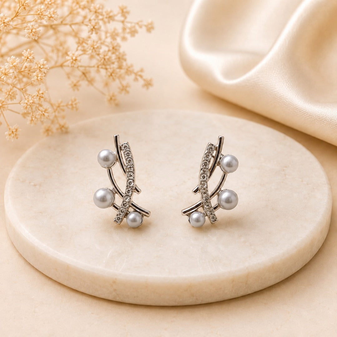 Elegant pearl crystal crossover stud earrings for women featuring silver-tone metal, sparkling crystal accents, and three light gray pearls, displayed on a marble jewelry stand.