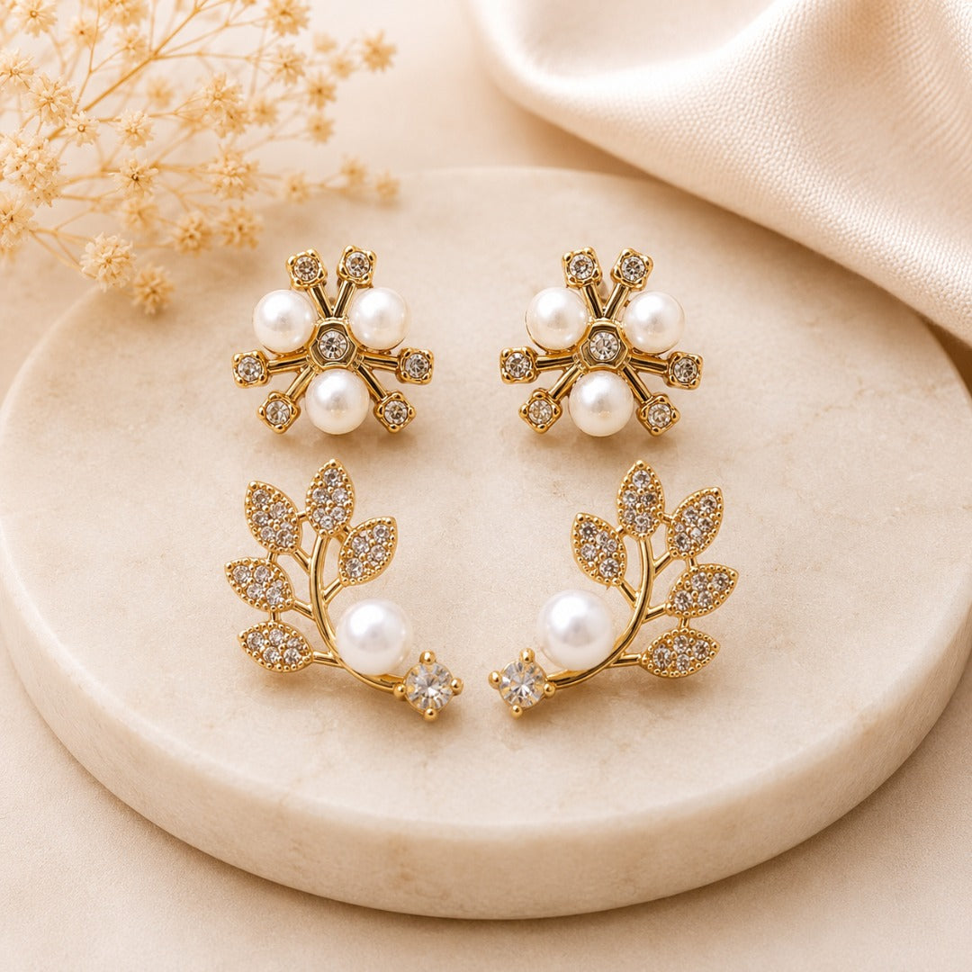 Close-up of elegant gold-tone floral and leaf stud earrings with sparkling CZ stones and faux pearls.