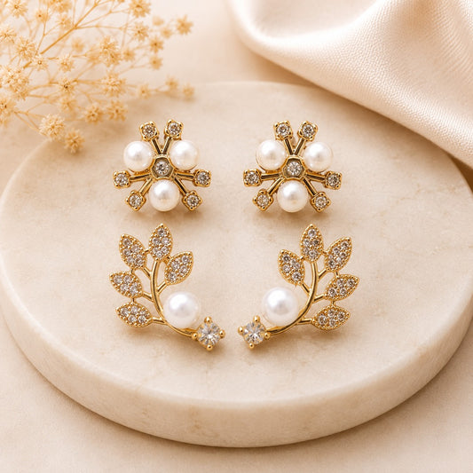 Close-up of elegant gold-tone floral and leaf stud earrings with sparkling CZ stones and faux pearls.