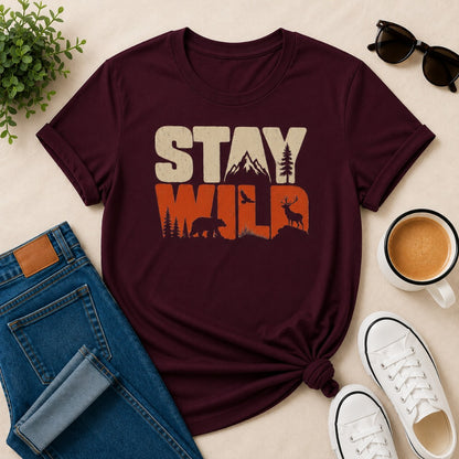 Women's maroon cotton T-shirt featuring a vintage Stay Wild wildlife graphic with mountains, bear, deer, pine trees, and birds.