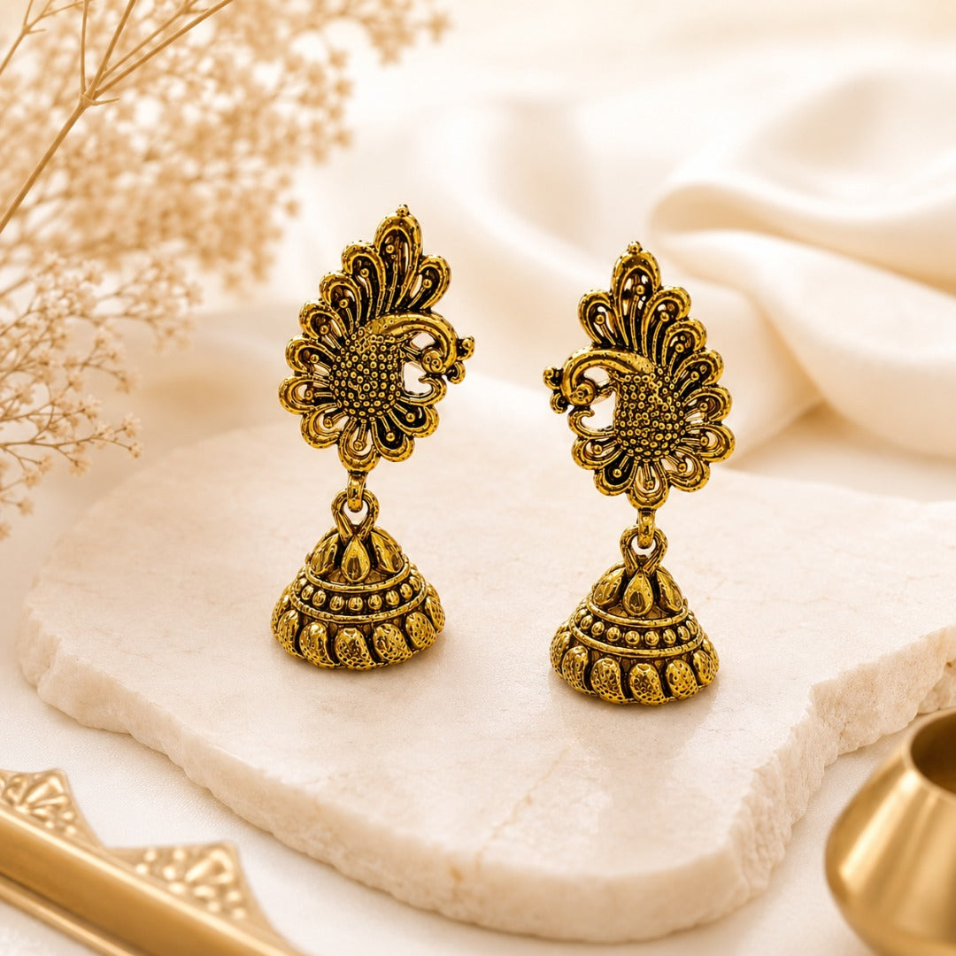 Antique gold traditional peacock floral jhumka earrings displayed on a marble surface