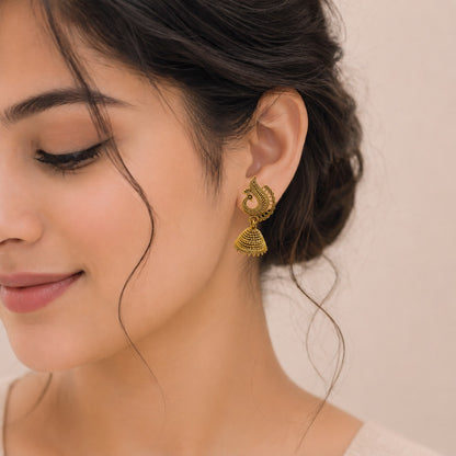 A close-up of a woman wearing traditional peacock jhumka earrings in antique gold finish with ethnic outfit